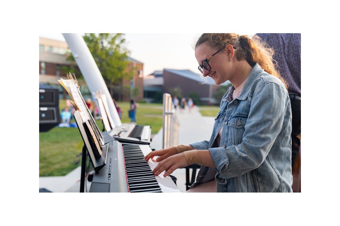 a student smiles and plays the piano at an outdoor concert