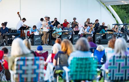 A crowd in lawn chairs listens to a jazz band perform at the outdoor Ender Pavilion