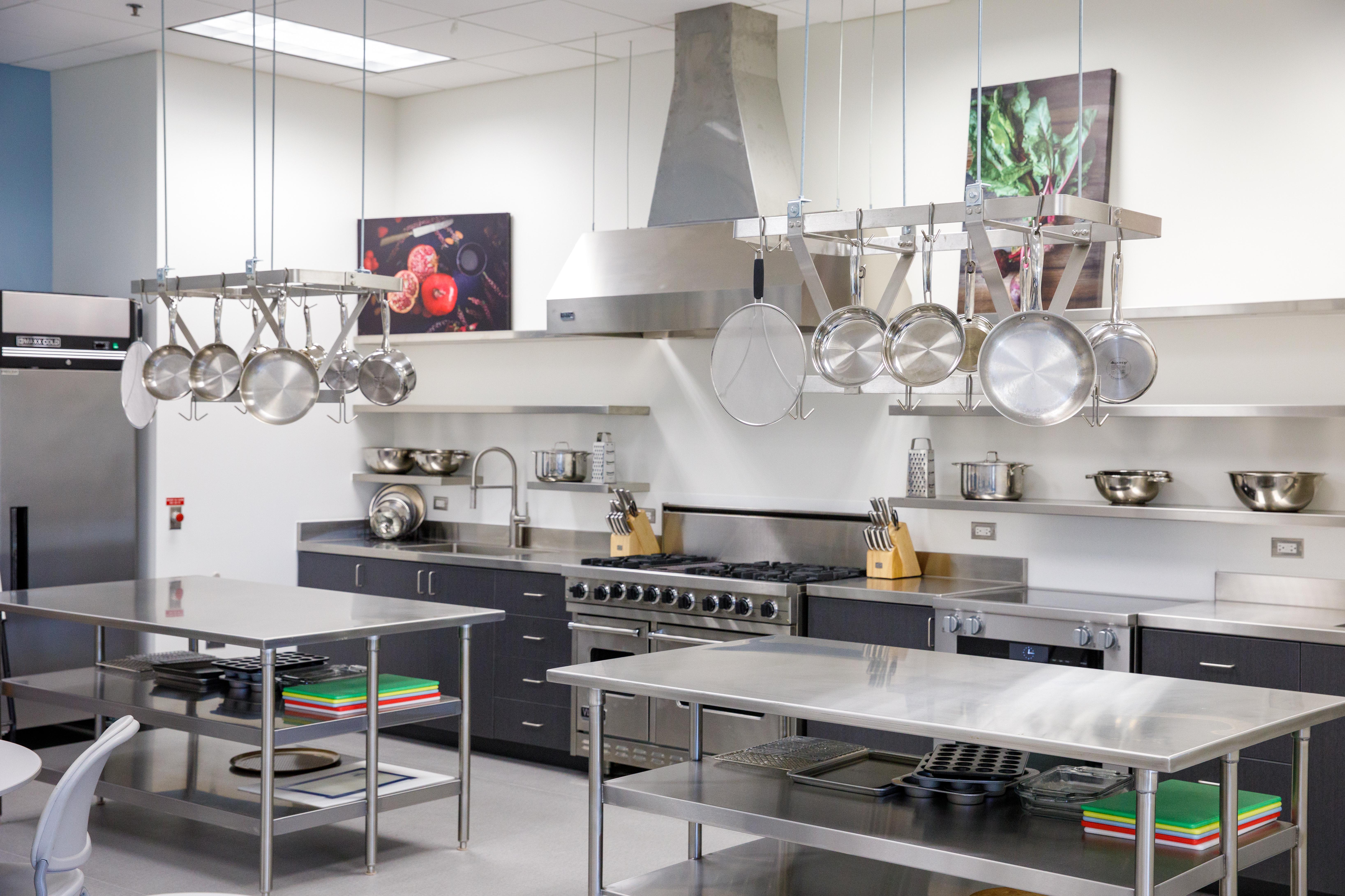 A clean, modern stainless kitchen area, complete with stainless steel prep tables and counters, pots and pans, a stove, knives