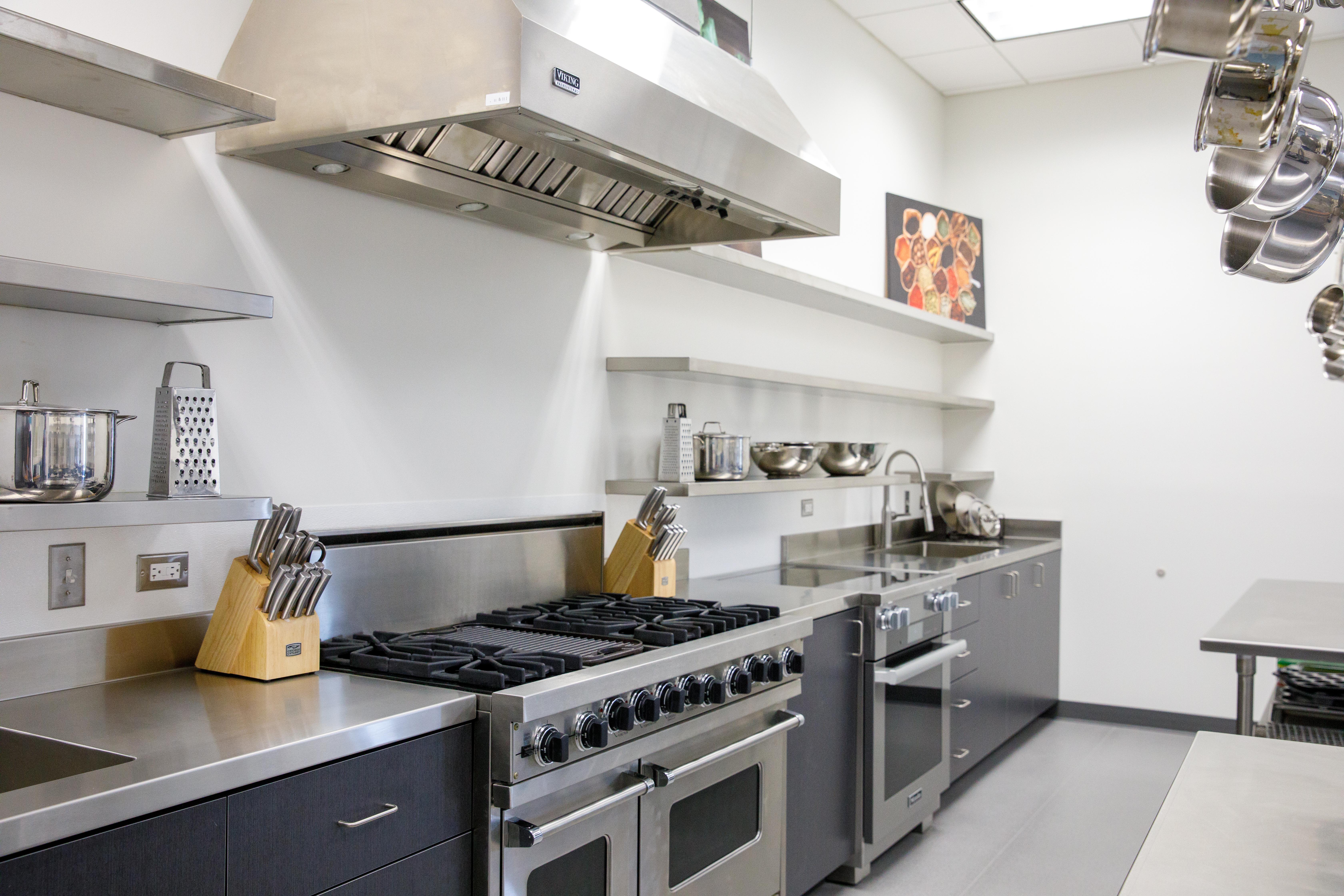 A closer look at the stainless steel stove, counter tops, shelving, and with cooking equipment, like a cheese grater.