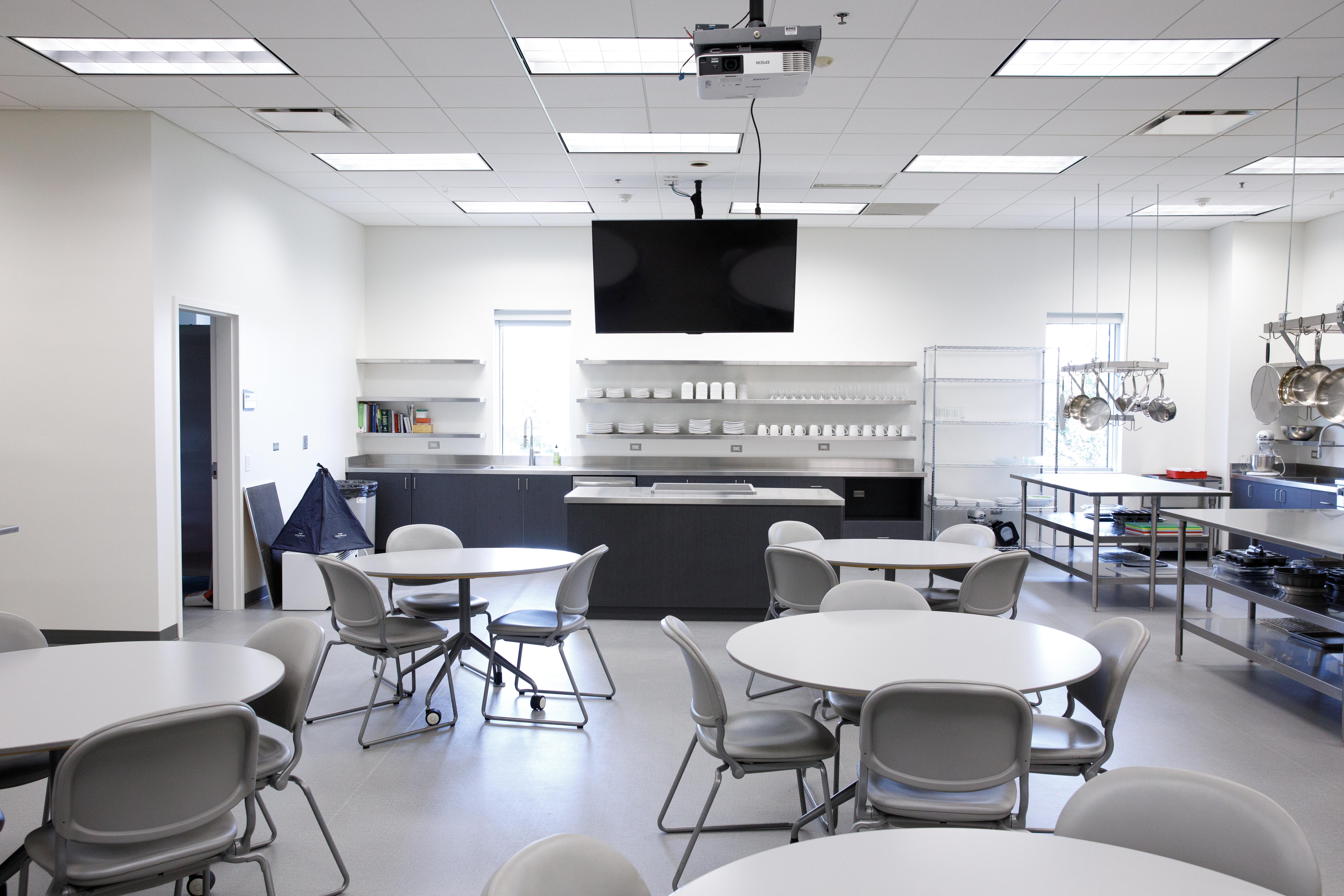 Several round tables and chairs are near the food preparation area in the Nutrition Lab