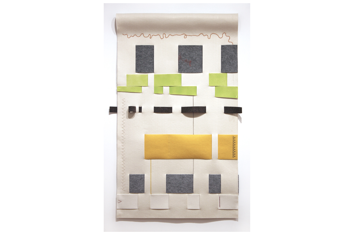 Large piece of beige felt rolled at the top with different colored pieces of felt in gray, green, and yellow woven through in large strips.  Decorative and functional stitching has been done.