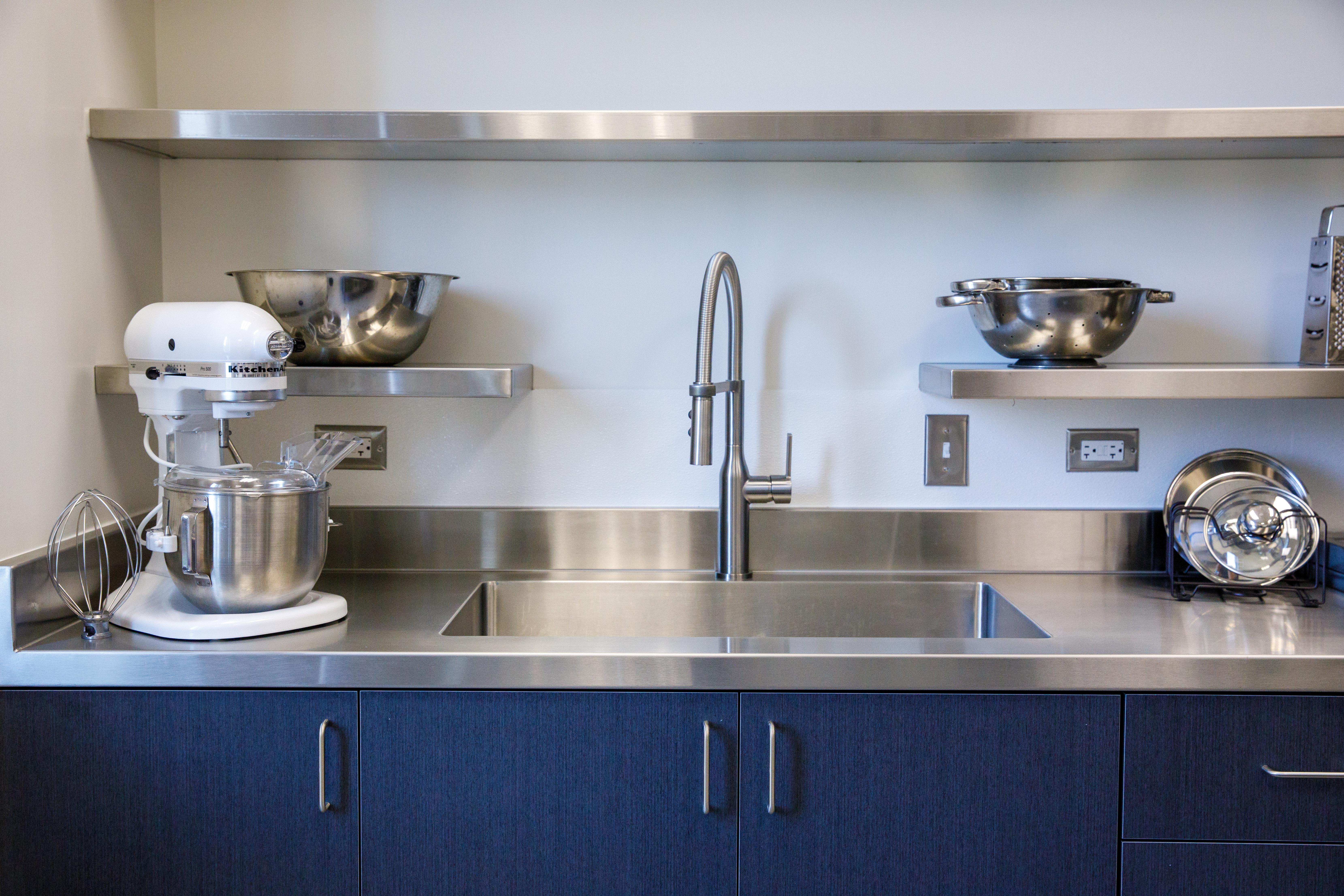 A close up view of the sink area, with stainless steel bowls on shelves, and a stand mixer on the counter.