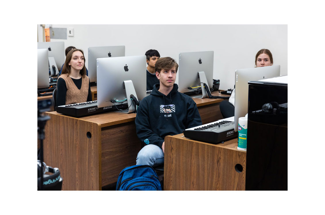 students sit in a classroom in front of computers with piano keyboards