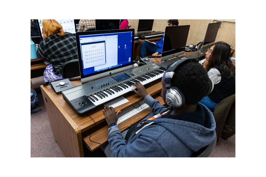 student wearing headphones sitting at a computer with a piano keyboard