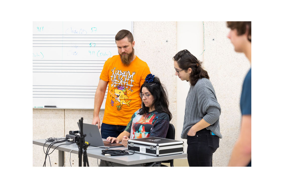 three students standing around a computer in a music classroom